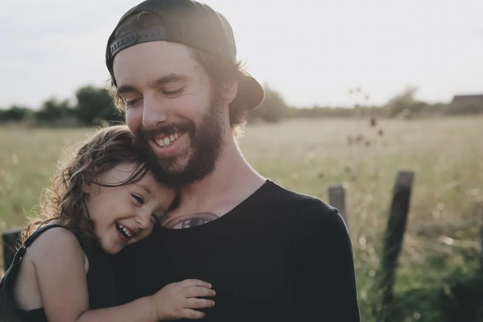 Pai e filha rindo abraçados ao ar livre